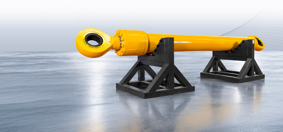 Yellow hydraulic cylinder with eye mounts supported horizontally on two black steel stands.